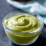 A close-up shot of a clear glass bowl filled with vibrant, creamy avocado sauce, artfully swirled on top.