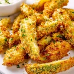 A white plate piled high with crispy golden Baked Avocado Fries, garnished with parsley, alongside a dipping sauce and lemon wedges.