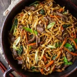 Close-up of a large black bowl filled with savory Beef Lo Mein, featuring tender beef strips, stir-fried noodles, vibrant carrots, and crisp snow peas.