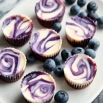 A white plate displays numerous blueberry swirl yogurt bites with vibrant purple patterns, surrounded by fresh blueberries.
