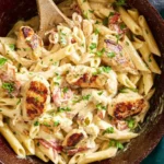 A close-up shot of creamy Cajun Chicken Alfredo pasta in a brown skillet with grilled chicken pieces, red peppers, and fresh parsley.