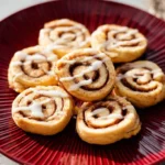 A vibrant red plate holds several delicious Cinnamon Roll Cookies, each topped with a white glaze drizzle.