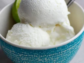 Three scoops of creamy white Coconut Lime Ice Cream in a turquoise speckled bowl, garnished with a fresh lime wedge.