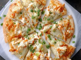 A delicious Crab Rangoon Pizza, cut into many slices, topped with shredded crab, orange sauce drizzles, and green onions, served with a side of dipping sauce.
