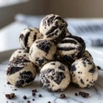 A delicious pile of homemade Cream Cheese Oreo Protein Balls, studded with dark cookie pieces, sits on a white marble plate.