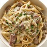A close-up shot of a bowl filled with Creamy Steak Pasta, garnished with fresh parsley, grated Parmesan cheese, and black pepper.