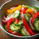 A vibrant Cucumber Sweet Pepper Salad in a bowl, featuring sliced cucumbers, red and yellow bell peppers, red onion, and fresh herbs.