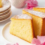 Slices of golden French Butter Cake dusted with powdered sugar, elegantly presented with a tea cup and pink flowers.