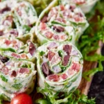 Close-up of several vibrant Greek Salad Pinwheels on a wooden board, garnished with fresh lettuce and a cherry tomato.