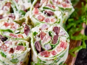 Close-up of several vibrant Greek Salad Pinwheels on a wooden board, garnished with fresh lettuce and a cherry tomato.