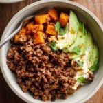 A rustic bowl of Ground Beef Hot Honey Bowls, featuring seasoned ground beef, roasted sweet potatoes, avocado, and creamy sauce.
