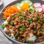 A vibrant ground turkey bowl with white rice, savory ground turkey, green onions, sesame seeds, fresh cucumbers, radishes, and a raw egg yolk.