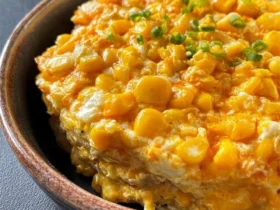 A close-up of a delicious Jalapeno-Corn Casserole topped with golden corn kernels, creamy sauce, and fresh green onions in a rustic bowl.