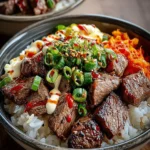 A vibrant Korean BBQ Steak Rice Bowl, featuring succulent steak cubes, white rice, green onions, sesame seeds, creamy sauce, and kimchi.