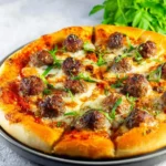 A delicious, golden-crusted Meatball Pizza topped with savory meatballs, melted mozzarella cheese, and fresh green herbs.