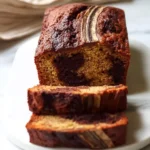 A freshly baked loaf of marbled Nutella Banana Bread, sliced and stacked on a white plate, with a banana slice garnish.