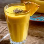 A vibrant Pineapple Banana Turmeric Smoothie in a glass, garnished with a pineapple slice and chia seeds on a wooden table.