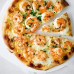 An overhead view of a freshly baked Shrimp Pizza topped with plump cooked shrimp, melted mozzarella cheese, and chopped green herbs.