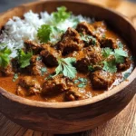 A wooden bowl brimming with a rich Slow Cooker Indian Beef Curry, accompanied by fluffy white rice and fresh cilantro.