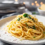 A close-up shot of a plate of creamy Spaghetti Alla Nerano, generously topped with grated cheese and fresh green herbs on a white plate.