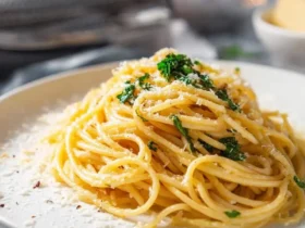 A close-up shot of a plate of creamy Spaghetti Alla Nerano, generously topped with grated cheese and fresh green herbs on a white plate.
