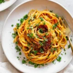 A plate of delicious Caramelized Shallot Pasta garnished with fresh parsley and grated cheese, presented with a golden fork.