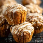 A stack of delicious Carrot Cake Muffins, generously drizzled with white icing, resting on a dark wire cooling rack.