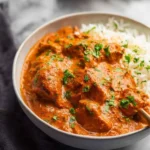 A close-up of a bowl filled with rich, creamy Chicken Tikka Masala alongside fluffy white rice, garnished with fresh cilantro.