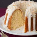A slice removed from a delicious Coconut Bundt Cake with Coconut Glaze, generously topped with toasted coconut flakes.