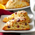Close-up of two Cranberry Orange Sour Cream Scones on a white plate, drizzled with glaze and topped with cranberries.