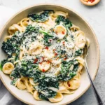 A close-up overhead shot of a bowl of creamy kale pasta, garnished with grated cheese and red pepper flakes.