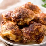A close-up shot of several perfectly cooked, golden-brown Crispy Baked Chicken Thighs seasoned with spices on a white plate.
