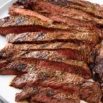 Close-up of perfectly sliced, juicy Grilled Skirt Steak on a white plate, seasoned with herbs and showing grill marks.