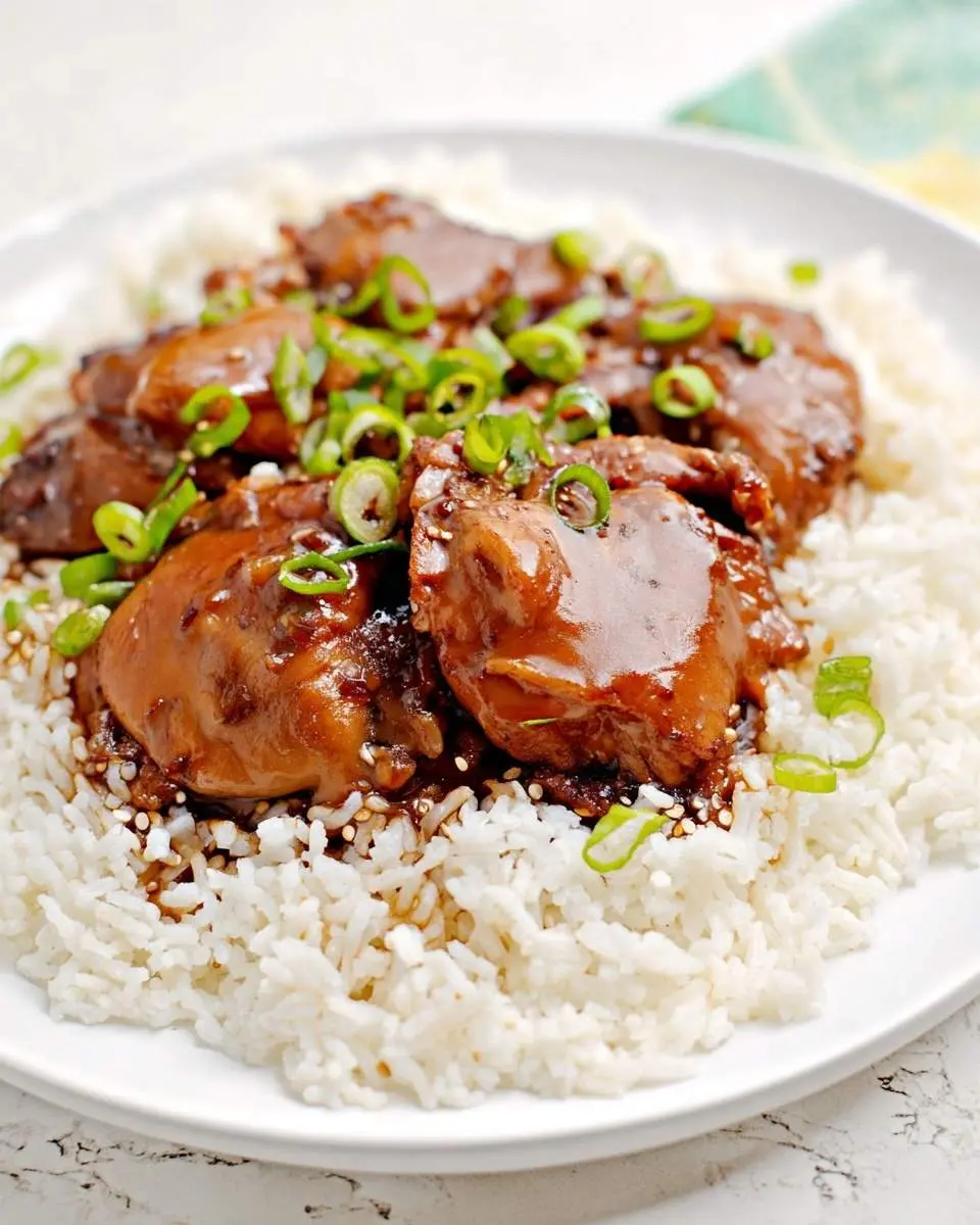 Hawaiian Shoyu Chicken 29 Glistening Hawaiian Shoyu Chicken thighs on a bed of white rice, garnished with fresh green onions and sesame seeds, on a white plate.