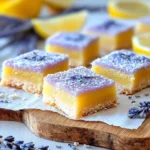 Close-up of square lavender lemon bars with bright yellow and light purple layers, dusted with powdered sugar and lavender sprigs.