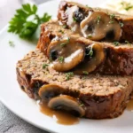 Slices of savory Meatloaf With Mushroom gravy and fresh thyme, served on a white plate, highlighting a hearty meal.