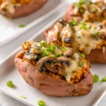 Delicious mushroom stuffed sweet potatoes topped with melted cheese and fresh green onions, served on white rectangular plates.