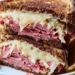 A close-up shot of a deliciously grilled Reuben Pastrami Sandwich, cut in half, showcasing layers of meat, melted cheese, and sauerkraut on rye bread.