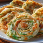 Golden-brown Rice Paper Scallion Pancakes on a white plate, showcasing their crispy texture and visible green scallion spirals.