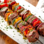 Juicy grilled Skirt Steak Kabobs with colorful bell peppers, zucchini, and red onions, drizzled with herbs on a white platter.