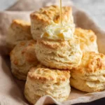 A stack of golden brown Sourdough Discard Biscuits topped with butter and a stream of honey being poured over them.