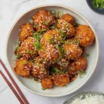 A close-up of delicious Sticky Sesame Cauliflower in a bowl, garnished with sesame seeds and green onions, ready to eat with rice.