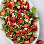 A vibrant Strawberry Goat Cheese Salad in a white bowl, featuring fresh strawberries, crumbled goat cheese, mixed greens, cucumber, and mint.