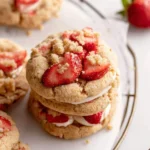 A close-up of a stack of three delicious Strawberry Shortcake Cookies with fresh strawberries and crumb topping.
