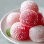 A white plate filled with perfectly round, powdered pink and red mochi, offering a delightful vision of Watermelon Mochi Joy.