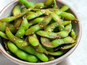 A rustic bowl filled with vibrant green edamame pods, seasoned with spices and sesame seeds, ready as delicious Air Fryer Edamame.