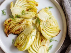 Perfectly cooked Air Fryer Fennel wedges, golden brown and garnished with fresh dill, served on a white plate.