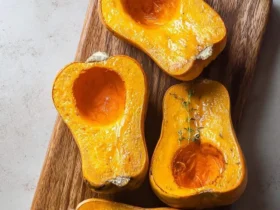 Four vibrant halves of golden Air Fryer Honeynut Squash, seasoned with fresh thyme, resting on a wooden board.