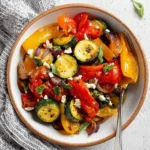 A close-up of a bowl filled with colorful Air Fryer Mediterranean Vegetables, including zucchini, bell peppers, and red onion, garnished with feta cheese and fresh herbs.