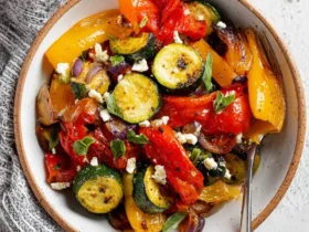 A close-up of a bowl filled with colorful Air Fryer Mediterranean Vegetables, including zucchini, bell peppers, and red onion, garnished with feta cheese and fresh herbs.